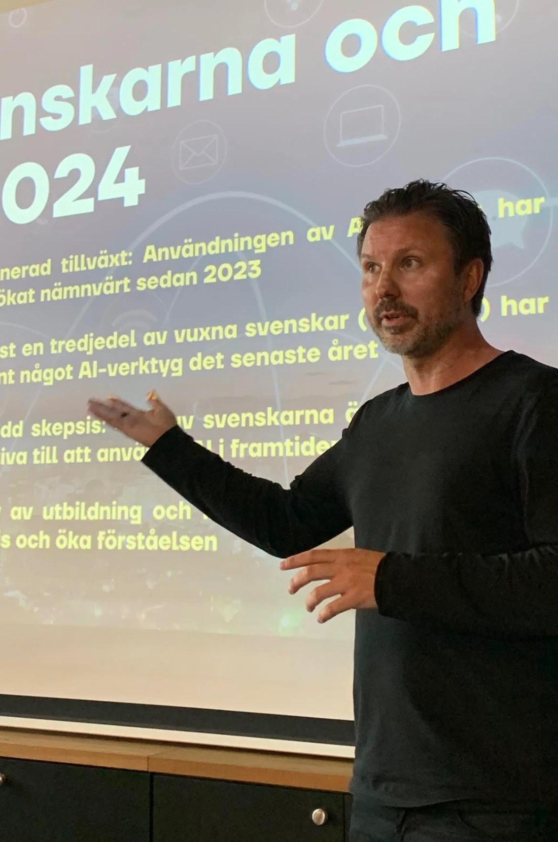 Mathias Karlsson framför en presentation om svenskarna och AI, mitt i en gest mot duken