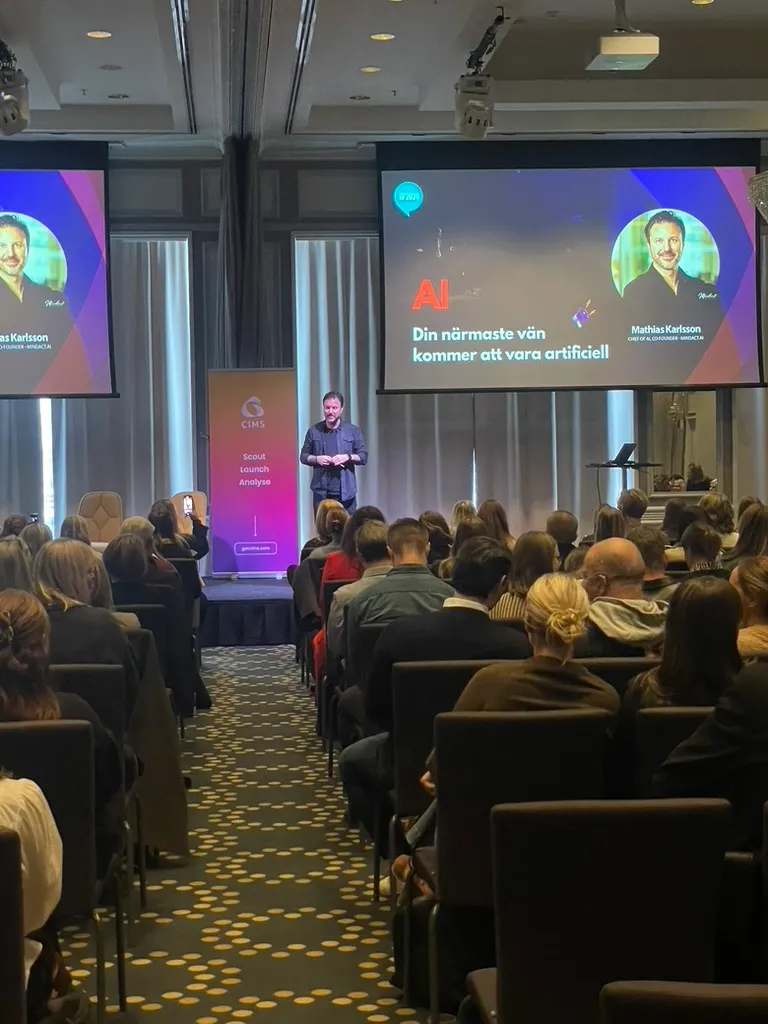 Fullsatt sal med Mathias namn och rubriken ”Din närmaste vän kommer att vara artificiell” på två storbildsskärmar
