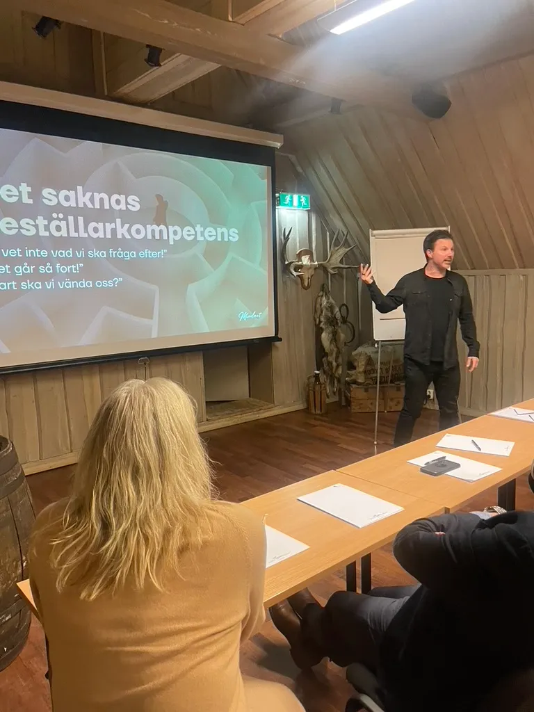 Mathias föreläser i en träpanelad sal med älghuvud på väggen, framför sliden ”Det saknas beställarkompetens”